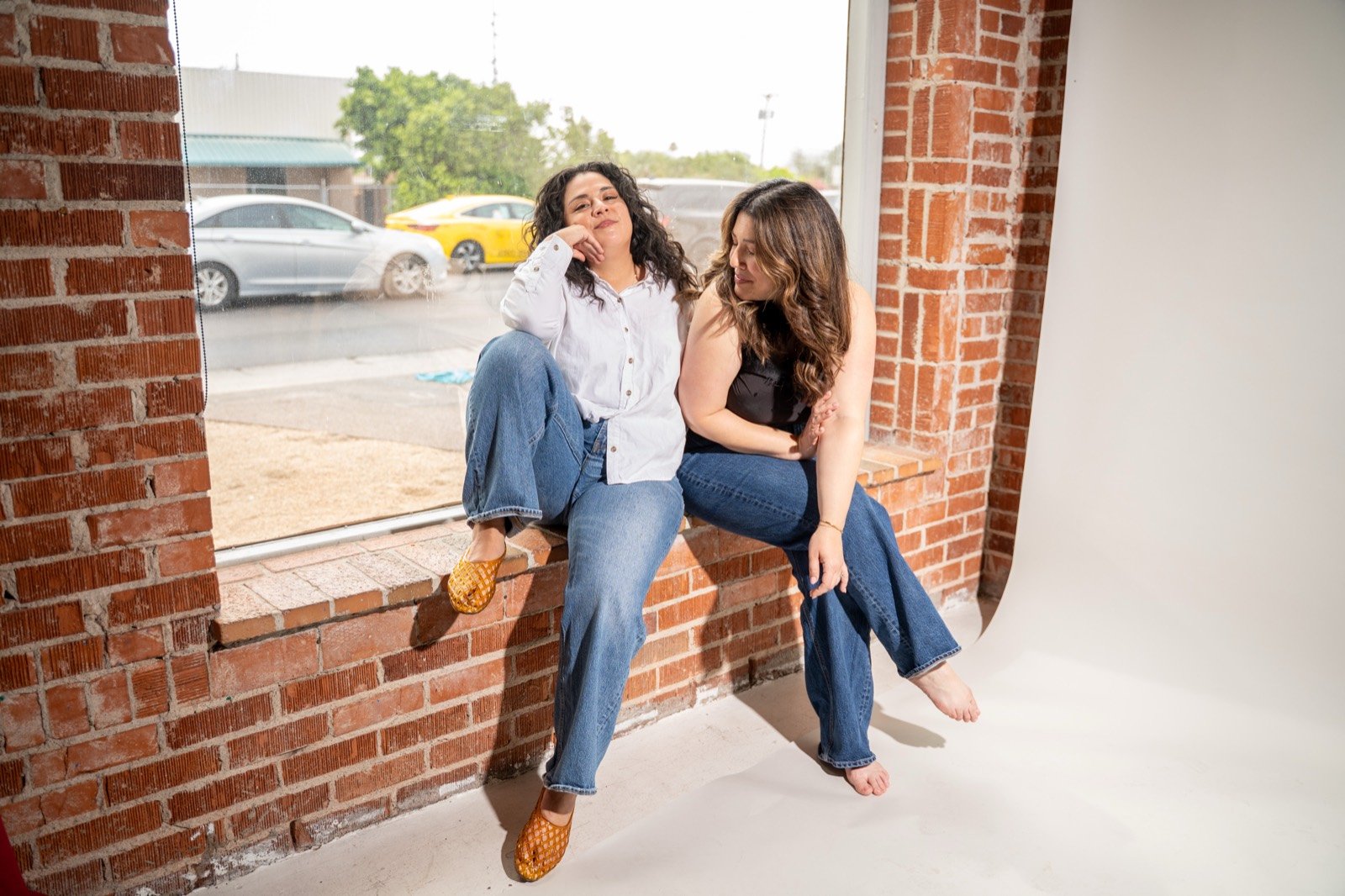 Alisha and Corinna sitting in a sunny brick window frame