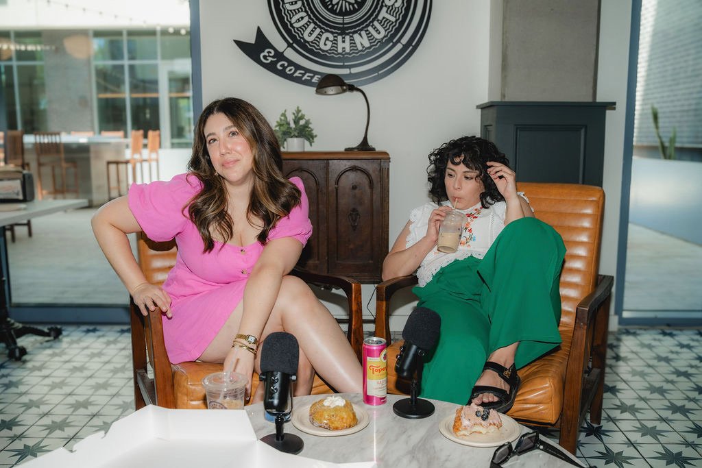 Alisha and Corinna recording in a coffee shop with mics, iced coffee, and doughnuts